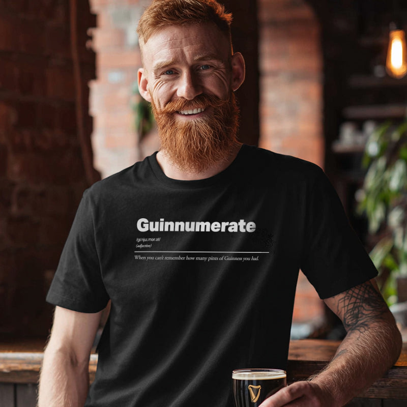Man wearing a black t-shirt with humorous text saying Guinnumerate holding a pint glass in a bar setting.