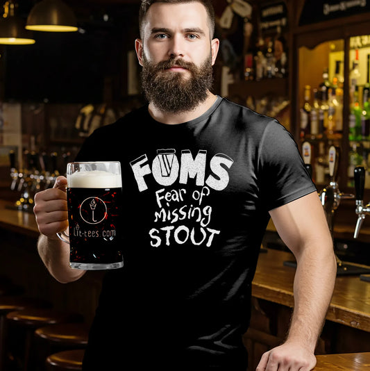 Man holding a glass of dark beer wearing a black t-shirt with 'FOMS Fear of Missing Stout' text in a bar setting.