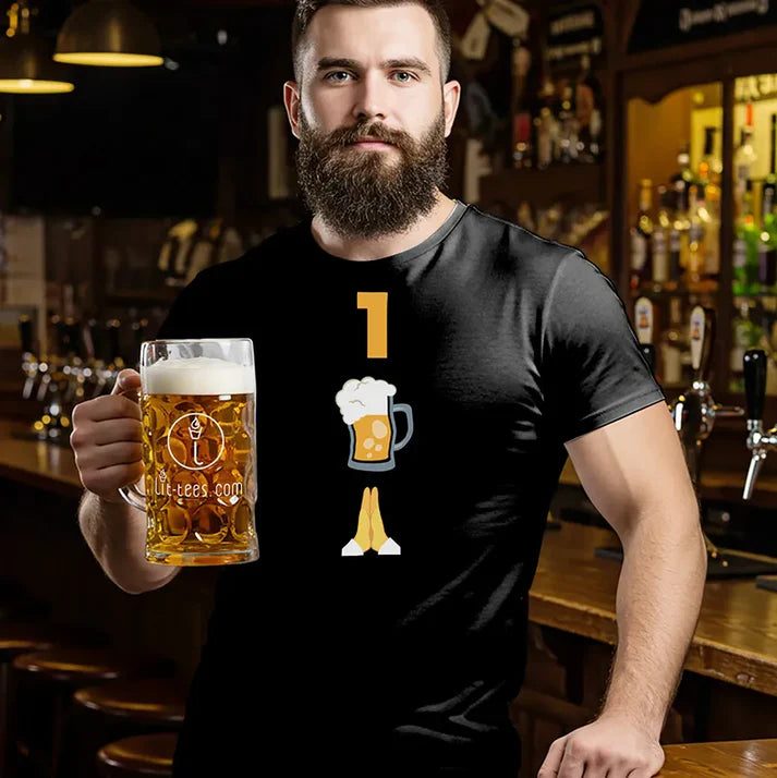 Man standing in a bar holding a beer wearing a black t-shirt with a graphic emoji themed design of '1 Beer Please' 