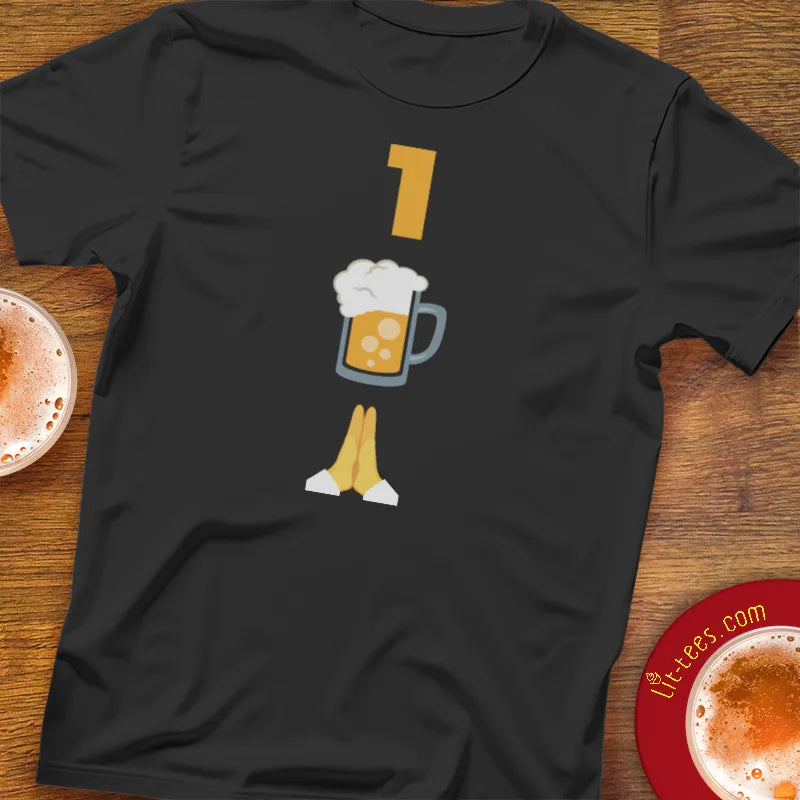 Black t-shirt with a graphic emoji themed design of 1 Beer Please on a bar table
