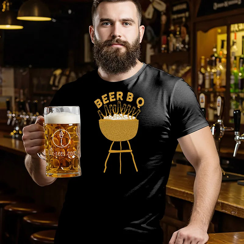 Man holding a beer mug wearing a black t-shirt with a graphic design reading Beer B Q in a bar setting