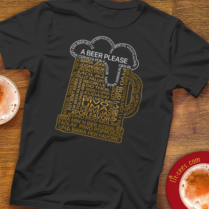 Black t-shirt with a graphic of a beer mug and 'A Beer Please' text in multiple languages on a wooden bar table.