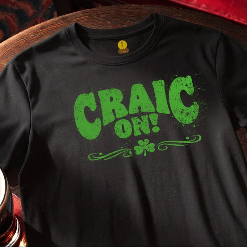 Black t-shirt with green 'CRAIC ON!' text and shamrock on a wooden surface.