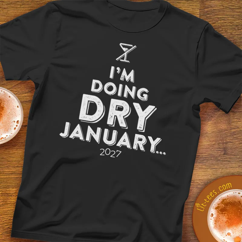 Black t-shirt with 'I'm doing Dry January 2027' text on a wooden bar table with drinks