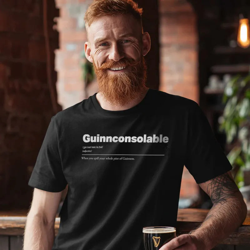 Man wearing a black t-shirt with 'Guinnconsolable' text, holding a pint glass in a bar setting.
