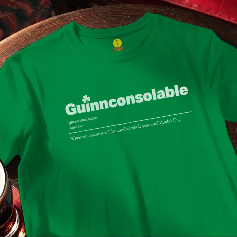 Green t-shirt with 'Guinnconsolable' text on a wooden bar surface