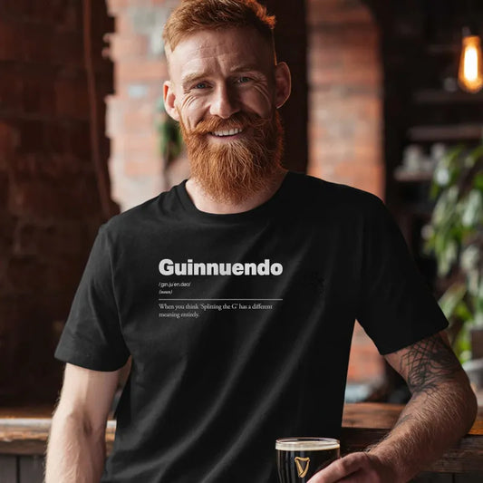 Man wearing a black t-shirt with 'Guinnuendo' text, holding a glass in a bar setting.