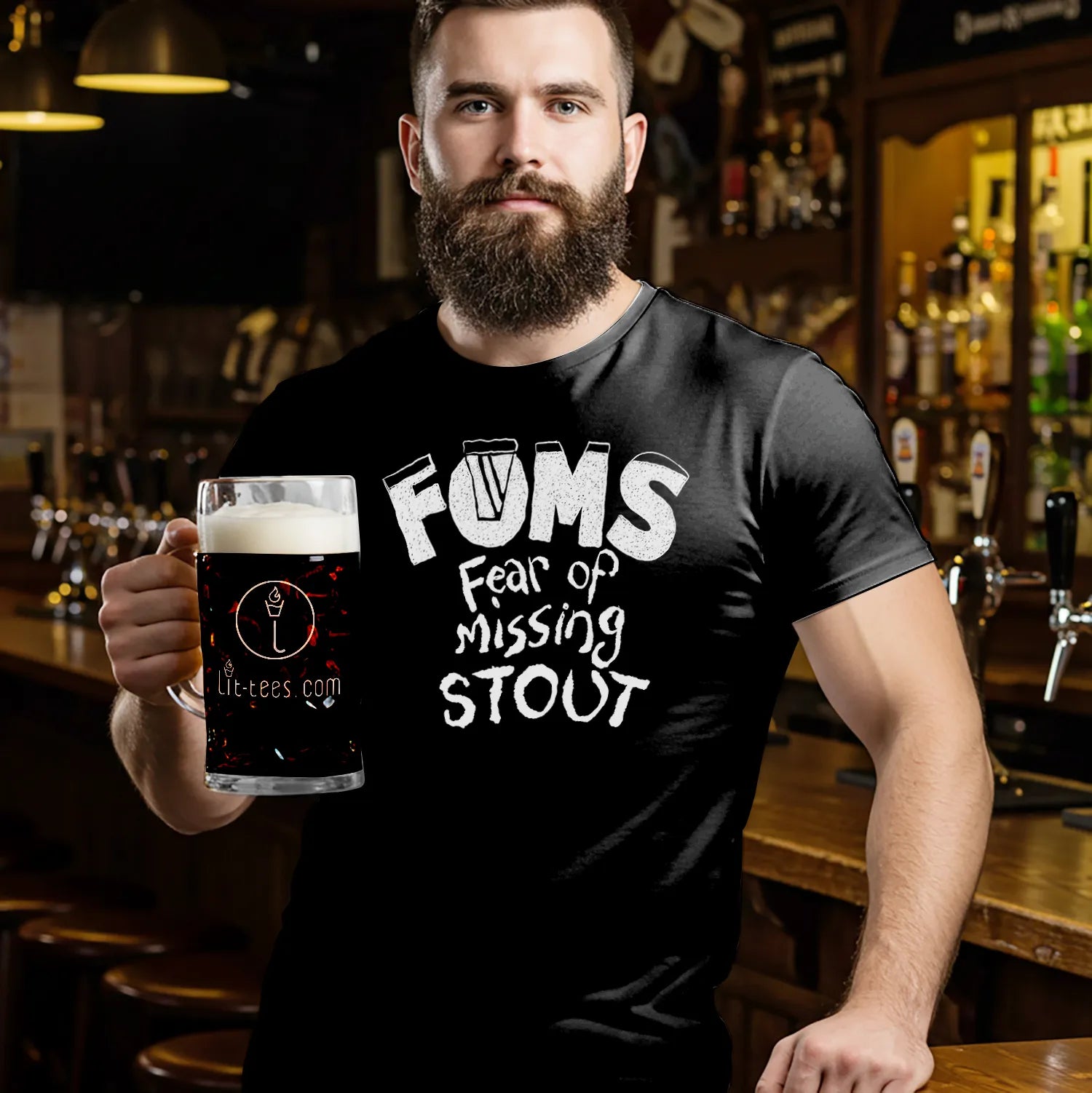 Man holding a glass of dark beer wearing a black t-shirt with 'FOMS Fear of Missing Stout' text in a bar setting.