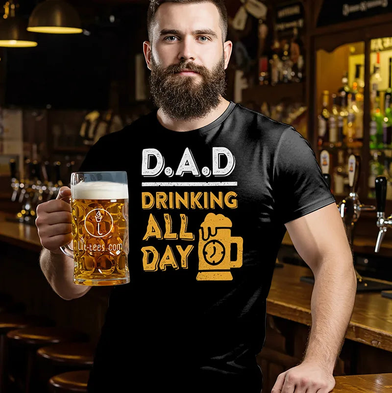 Man holding a beer mug wearing a black t-shirt with 'DAD Drinking All Day' text in a bar setting.