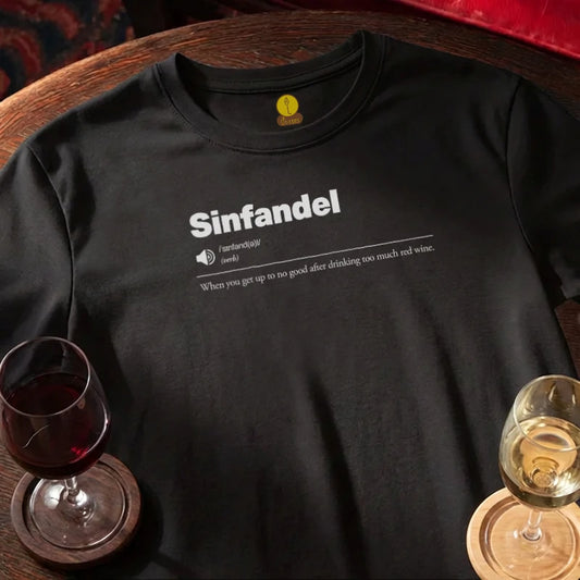 Black t-shirt with 'Sinfandel' definition print, wine glass, and glass on a wooden bar surface.