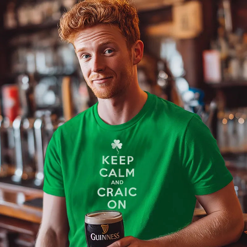 Man wearing a green t-shirt with 'Keep Calm and Craic On' holding a pint of Guinness in a  bar setting.